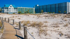 Un hotel frente a la playa con un paseo marítimo de madera que conduce a la entrada, con varios pisos y balcones.