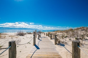 Un muelle de madera que lleva a una playa, con cielo despejado.
