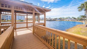 A wooden deck with a view of a body of water and a building in the background. - Mariner Lakes 40 2 Bedroom Condo (Orange Beach)