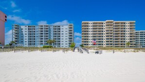 A beachfront hotel with multiple floors, a sandy beach in the foreground, and a clear blue sky. - Mariner Lakes 40 2 Bedroom Condo (Orange Beach)