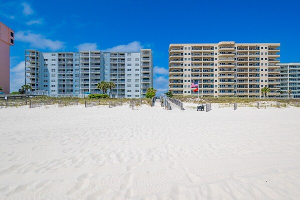 A beachfront hotel with multiple floors, a sandy beach in the foreground, and a clear blue sky.
