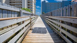 A wooden boardwalk leading to a high-rise building with multiple balconies. - Mariner Lakes 40 2 Bedroom Condo (Orange Beach)
