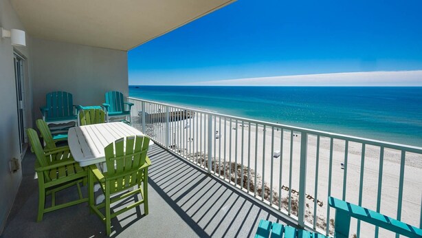 A balcony with a view of the ocean, green chairs, a table, and a white railing.