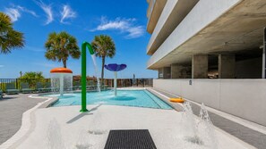 A swimming pool area with a water fountain, benches, and palm trees.