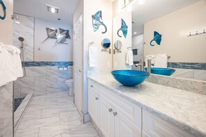 A modern bathroom with a large blue glass bowl sink, white marble countertops, and a shower with a glass door. - Seawind 809 3 Bedroom Condo (Gulf Shores)