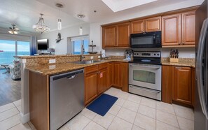 A modern kitchen with granite countertops, stainless steel appliances, wooden cabinets, and a view of the ocean. - Seawind 809 3 Bedroom Condo (Gulf Shores)