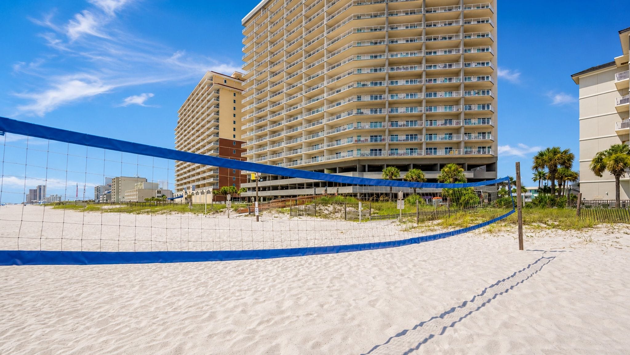 A beach volleyball court with a net, sand, and a tall hotel building in the background.