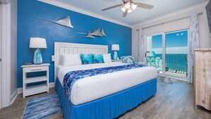 A bedroom with a bed, a nightstand, a lamp, a ceiling fan, and a view of the outside.
