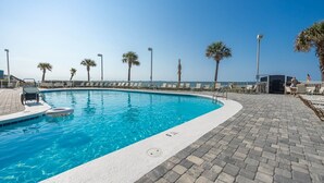 A swimming pool with a paved deck, lounge chairs, and palm trees.