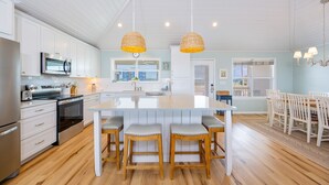 Uma cozinha moderna com armários brancos, eletrodomésticos de aço inoxidável, uma ilha central com banquetas e iluminação pendente.