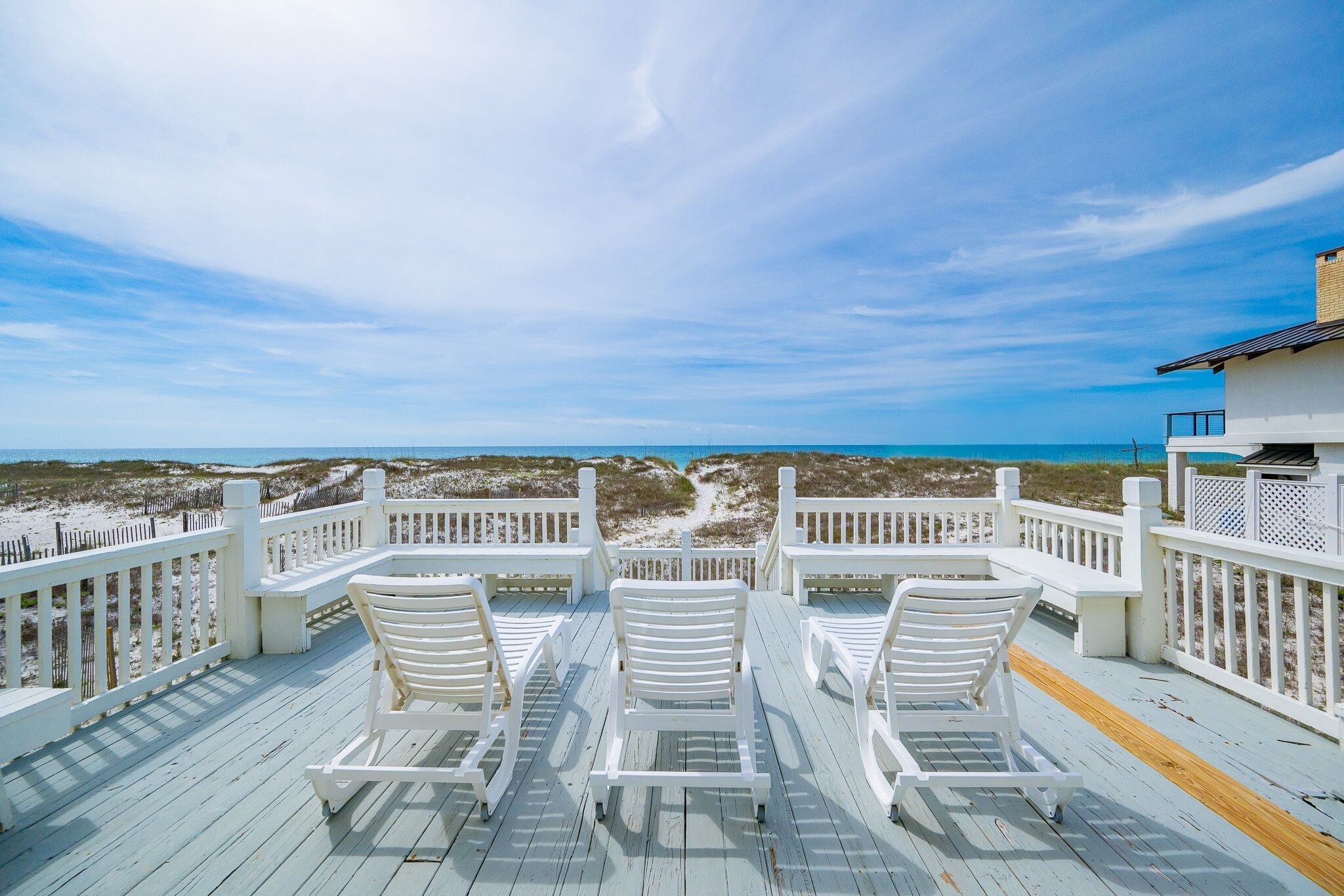 A deck with white chairs and a view of the beach.