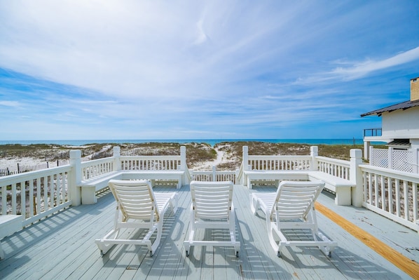 A deck with white chairs and a view of the beach.