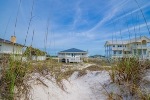 A beachfront property with a covered patio, a large house with a balcony, and a smaller building with a covered deck.