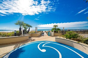 Un sentier menant à une plage bordée de palmiers et dotée d’une piste cyclable bleue.