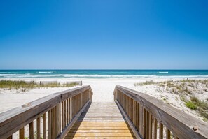 Une promenade en bois qui mĂšne Ă une plage de sable bordĂ©e par lâocĂ©an.