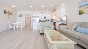 A modern living room with a glass coffee table, a sofa, and a dining area with white chairs.