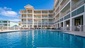 A hotel with a swimming pool, multiple balconies, and a clear blue sky.