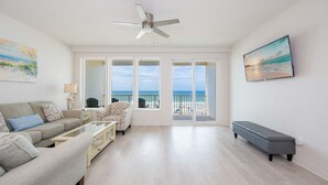 A spacious living room with a large window, a ceiling fan, a sofa, a coffee table, and a bench.