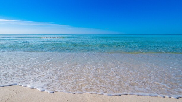 A beach with clear blue water and a sandy shore.