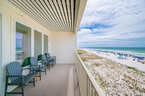 En balkon med stole og udsigt til en strand med parasoller og mennesker.