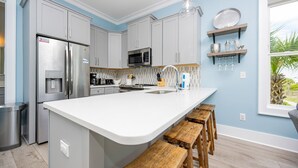 A modern kitchen with grey cabinets, a stainless steel refrigerator, a microwave, and a white island with wooden stools.