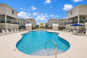 A swimming pool surrounded by lounge chairs and umbrellas, with a clear sky above. - West Side Cottages U 3 Bedroom Home (Gulf Shores)