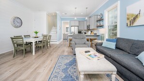 A modern living room with a grey sofa, a dining table with chairs, and a kitchen in the background.