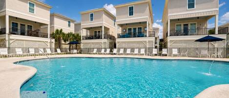 A swimming pool surrounded by multi-story buildings with balconies, clear skies, and no visible people.