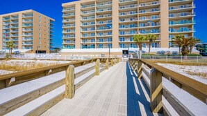 Un hôtel en bord de mer doté de nombreux balcons, d’une plage de sable et d’une promenade en bois menant à l’entrée.