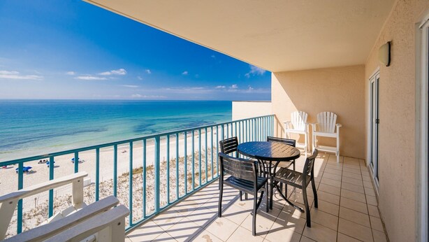 Un balcon avec vue sur l’océan, une table avec des chaises et une porte blanche.