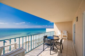 A balcony with a view of the ocean, a table with chairs, and a white door.