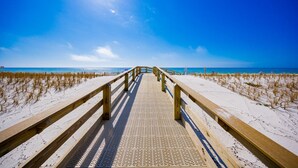 Une promenade en bois qui mène à une plage, avec un ciel dégagé.