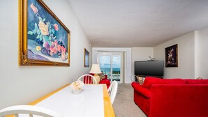 Ein Wohnzimmer mit Esstisch, rotem Sofa und Fernseher.