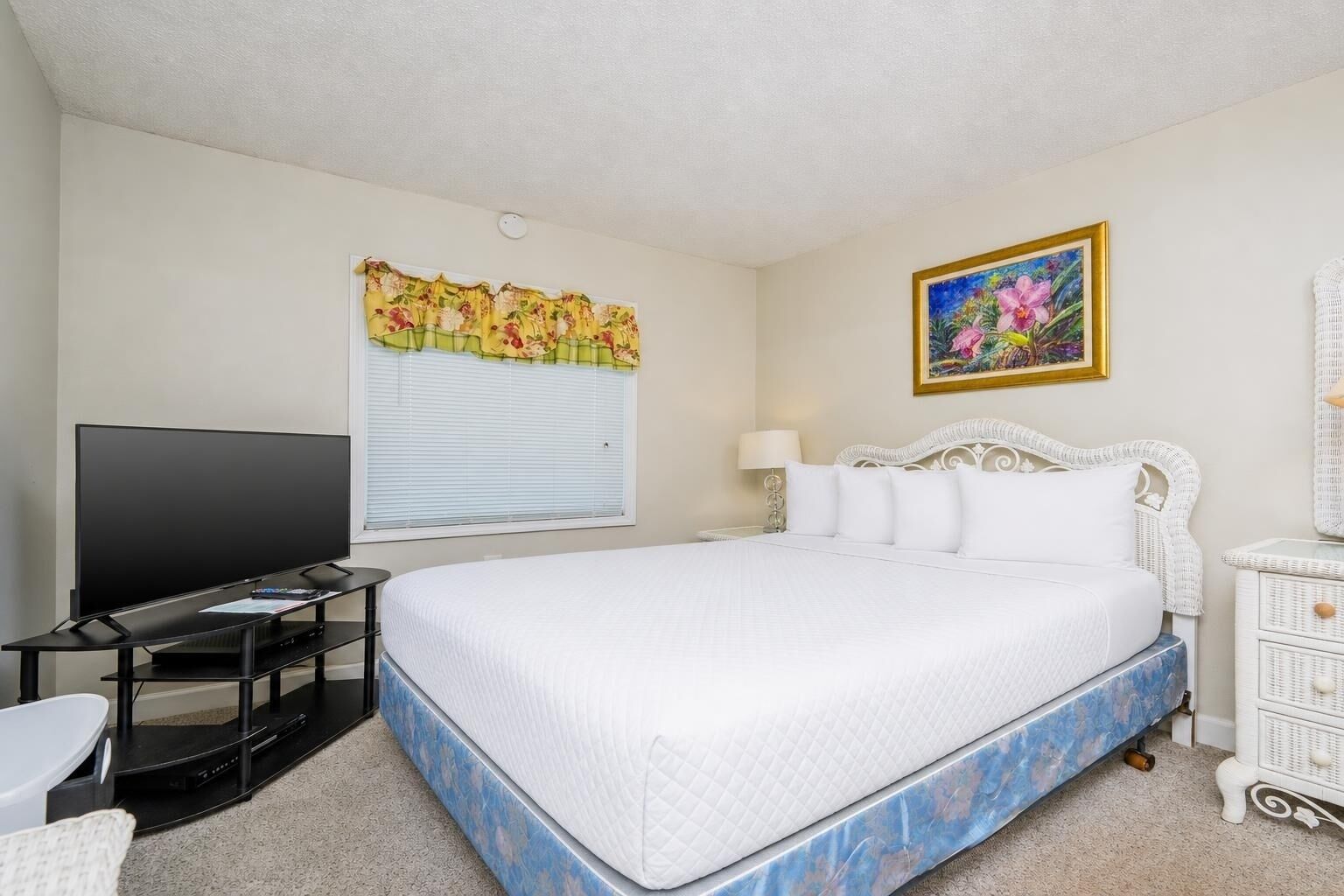 A hotel room with a bed, a television, a desk, and a window with blinds.