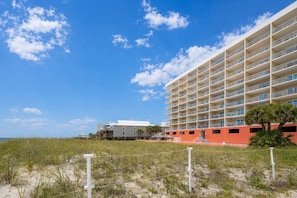 A beachfront hotel with multiple balconies, a sandy beach in the foreground, and a clear blue sky.