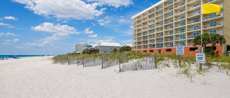 Ett hotell vid stranden med flera balkonger, en sandstrand och en klar himmel.