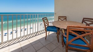 A balcony with a view of the beach, a round table, and wooden chairs with blue cushions. - Seacrest 805 1 Bedroom Condo (Gulf Shores)