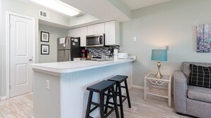 A modern kitchen with a central island, bar stools, a microwave, and a refrigerator. - Seacrest 805 1 Bedroom Condo (Gulf Shores)