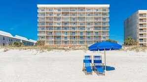 A beachfront hotel with multiple balconies, a sandy beach, and a blue umbrella. - Seacrest 805 1 Bedroom Condo (Gulf Shores)