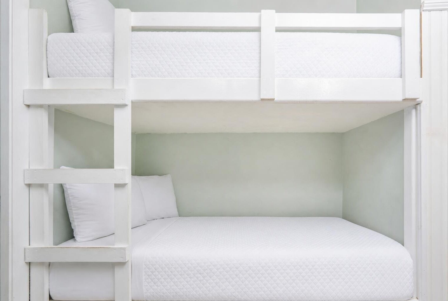 A bunk bed with a ladder, a single bed below, and a pillow on the lower bunk.