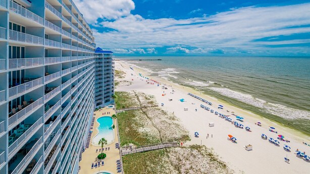 A high-rise hotel with multiple balconies overlooking a beach with umbrellas and lounge chairs. - Lighthouse 1417 1 Bedroom Condo (Gulf Shores)