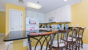 Una cocina con armarios blancos, un refrigerador, un microondas y un comedor con un taburete de bar y sillas.