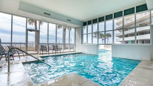 An indoor swimming pool with clear views of palm trees and a beach, surrounded by large windows and a poolside area with chairs. - Seawind 905 3 Bedroom Condo (Gulf Shores)