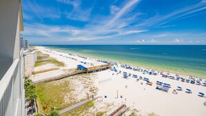 A beach with a long stretch of sand, a pier, and a building with a blue roof. - Seawind 905 3 Bedroom Condo (Gulf Shores)