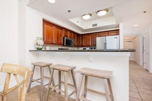 A kitchen with wooden cabinets, a black microwave, a white refrigerator, and a central island with stools.