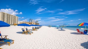A beach with rows of sun loungers and umbrellas, a hotel building, and the ocean in the background. - Seawind 905 3 Bedroom Condo (Gulf Shores)