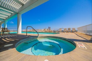 A swimming pool with a view of the beach and ocean, surrounded by lounge chairs and a covered area. - Colonnades 1201 4 Bedroom Condo (Gulf Shores)
