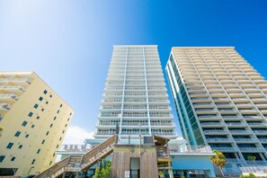 A high-rise building with multiple balconies, a staircase leading to the entrance, and adjacent buildings. - Colonnades 1201 4 Bedroom Condo (Gulf Shores)