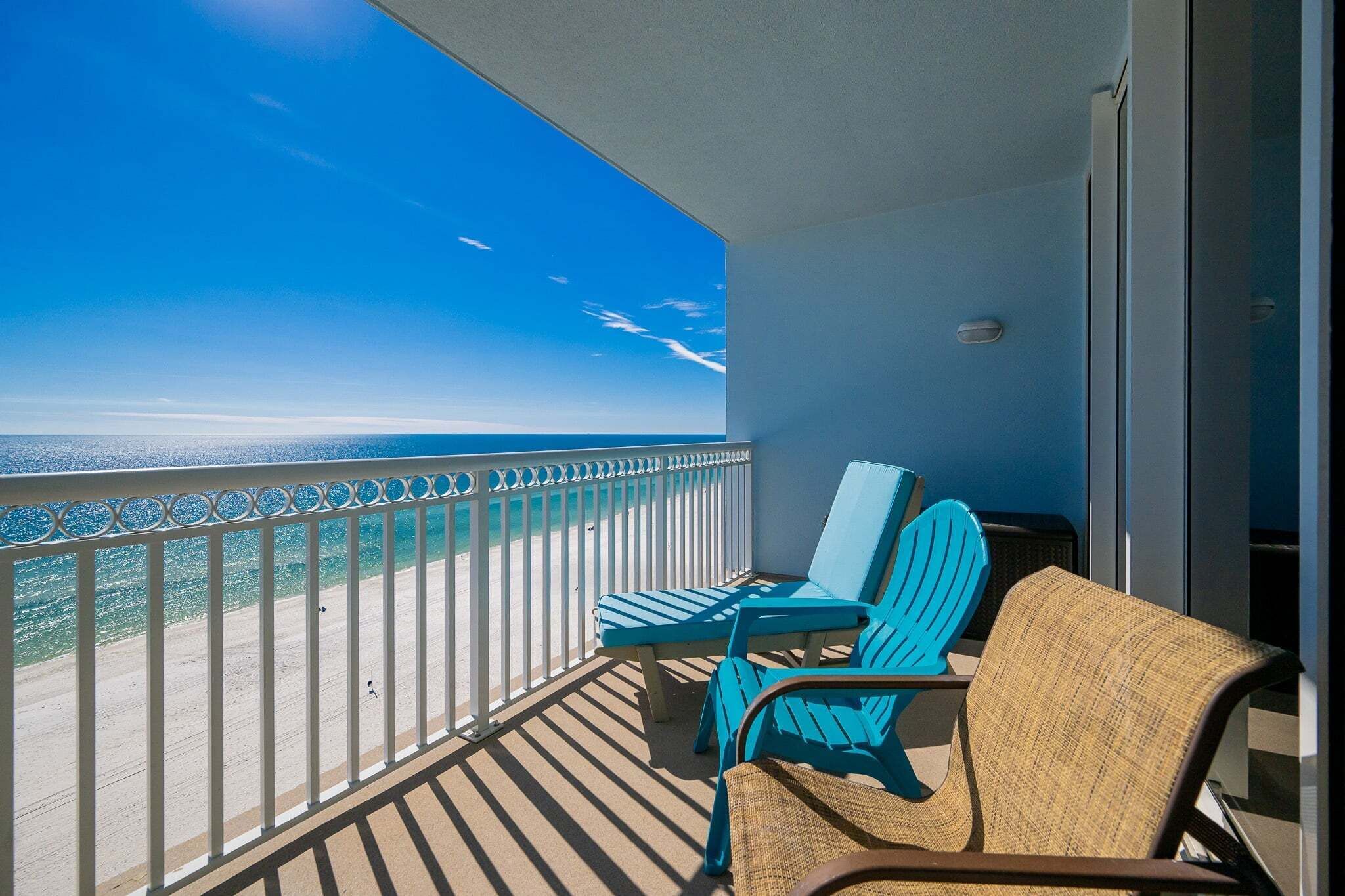 Een balkon met uitzicht op de oceaan, twee blauwe stoelen en een rieten stoel.