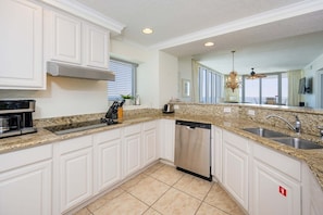 A modern kitchen with white cabinetry, granite countertops, stainless steel appliances, and a large window offering a view.